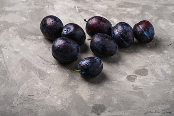 Fresh ripe plum fruits with water drops on stone concrete background, angle view