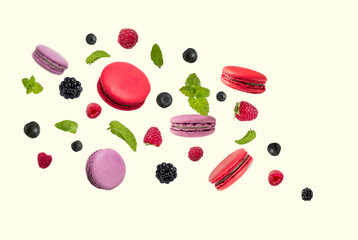 Yellow,  pink and red  french macaroons and berries with mint falling or flying in motion on a light yellow background.