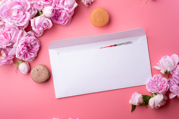  white envelope with cardaround roses and macaroons against  pink background. life style concept