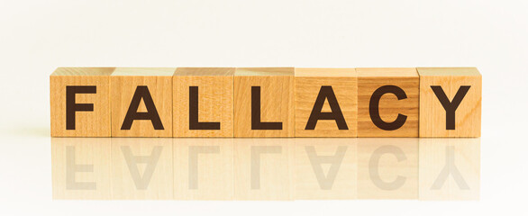 Wooden Blocks with the text: FALLACY. The text is written in black letters and is reflected in the mirror surface of the table. New business relaunch startup concept