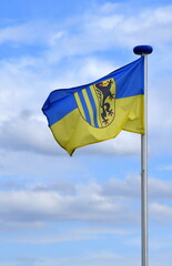 Im Wind wehendes Dresdner Stadtwappen auf einer blau-gelben Flagge vor strahlend blauem Himmel