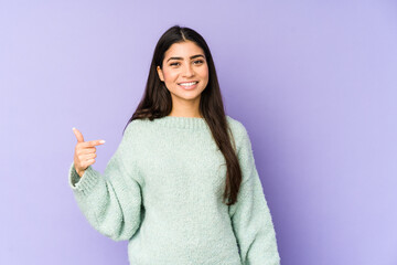 Young indian woman isolated on purple background person pointing by hand to a shirt copy space, proud and confident