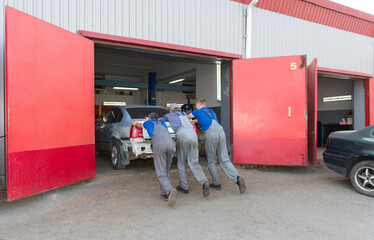 Three male workers push the car into the garage. Car service.