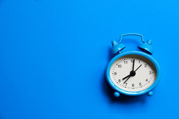 Alarm clock on a blue background top view flat lay with copy space. Minimalistic monochrome concept of time, deadline, work, morning.Selective focus.