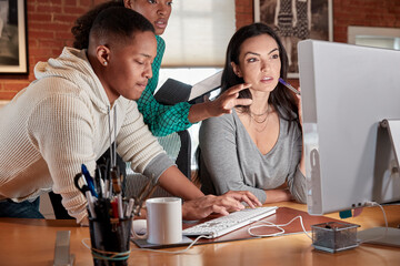 Group of young co-workers in office gathered around computer screen
