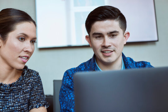 Young man and woman co-workers gathered around laptop computer looking at screen 