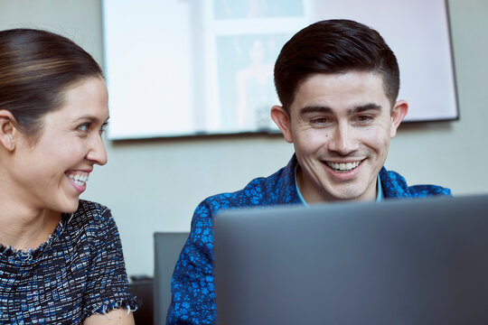 Young man and woman co-workers gathered around laptop computer laughing 