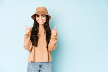 Obraz na płótnie Canvas Young indian woman wearing a hat isolated on blue background smiling and raising thumb up