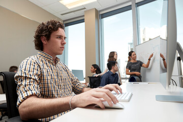 Young man using computer in office looking, co-workers having discussion in background 