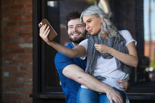 Young couple hanging out in front of cafe, using mobile phone to take a selfie 