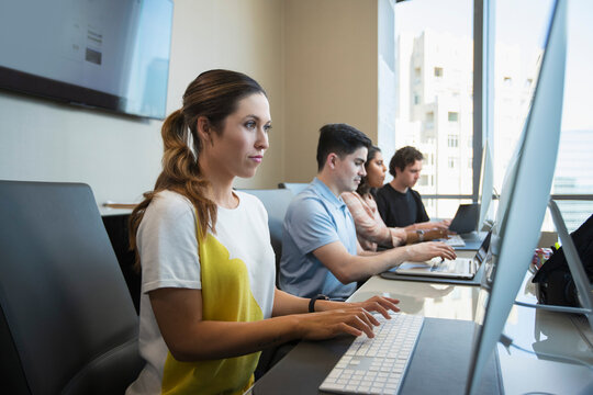 Young woman using computer in office typing on keyboard, co-workers working in background 