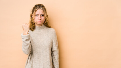 Young caucasian woman isolated on beige background showing fist to camera, aggressive facial expression.