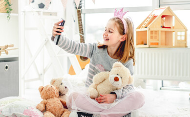 Happy little girl taking photo with toys in cute playroom