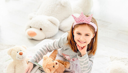 Fototapeta premium Adorable little girl in diadem with teddy bears in bright room