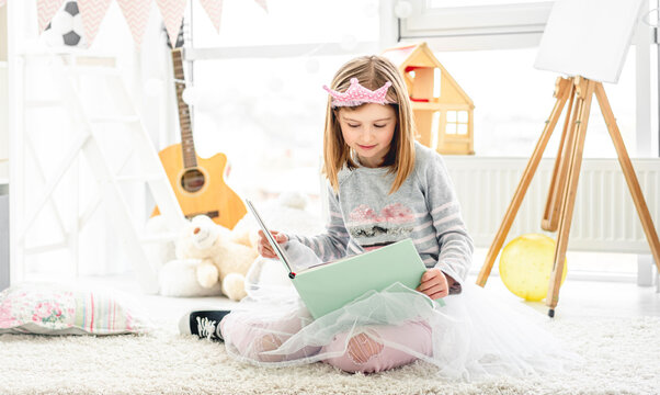 Beautiful little girl reading intersting book sitting on floor in children room