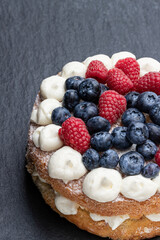 Victoria sponge cake with whipped cream and berries on top on stone background