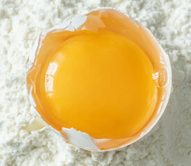 White egg and egg yolk on flour background, close up