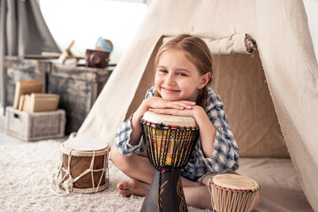 Cute little girl with ethnic drums sitting near wigwam in playroom © Ievgen Skrypko