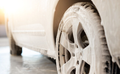 Obraz na płótnie Canvas Car wheel under washing foam during car wash, close up