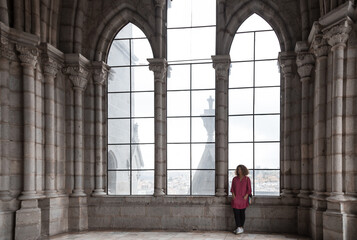Latin woman with red shirt and black pants standing behind amazing large windows in a cathedral	