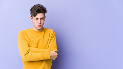 Young caucasian man isolated on purple background frowning face in displeasure, keeps arms folded.