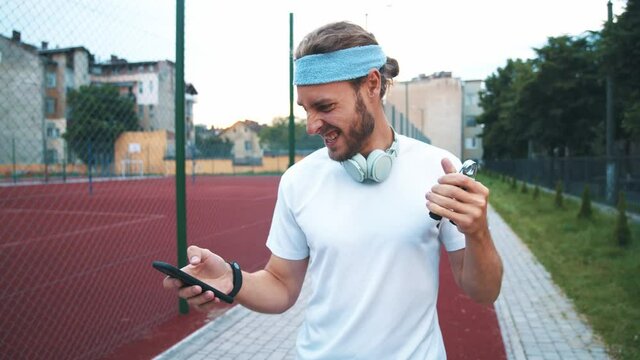 Funny scene of comical fit hipster training espander and typing smartphone as fast as he can. Multi-tasking in sports. Strong sportsman. Humor concept.