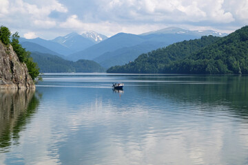 Pleasure boat on lake between hills covered with green forest