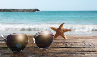 Starfish and stylish sunglasses on wooden table near sea
