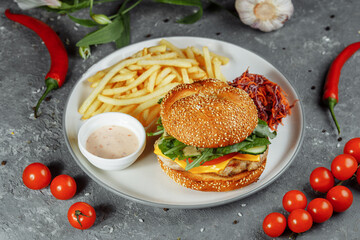 Turkey burger on a bun with cheese, lettuce, tomatoes and fresh cucumber. Burger with cutlet of turkey meat on a gray background with french fries