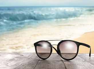 Fototapeta na wymiar Stylish sunglasses on wooden table near sea with sandy beach