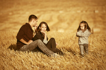 Naklejka na ściany i meble Happy young family with two year old baby girl in harvested field