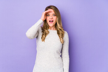 Young caucasian woman isolated on purple background shouts loud, keeps eyes opened and hands tense.