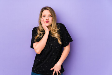 Fototapeta premium Young caucasian woman isolated on purple background blows cheeks, has tired expression. Facial expression concept.
