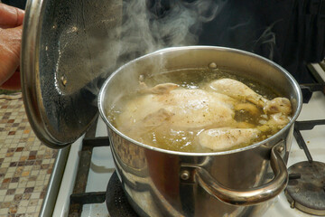  Chicken in boiling broth in a saucepan with the lid open.