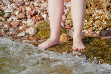    Female legs stand on a stone in front of the oncoming  wave.