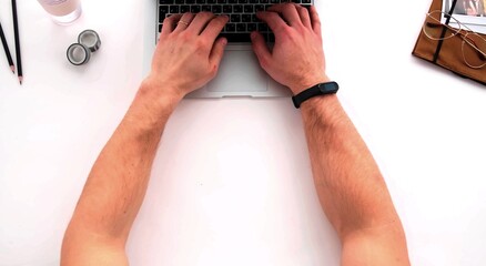 A top photo of the arms of a man who is writing on a keyboard