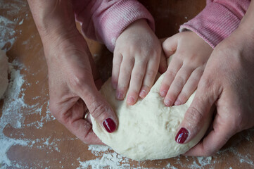 Hands of a little girl kneading dough for pizza with her mother