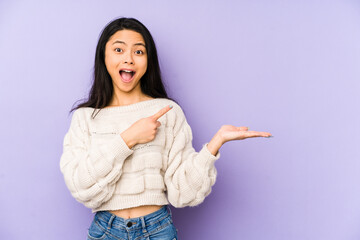 Young chinese  woman isolated on a purple background excited holding a copy space on palm.