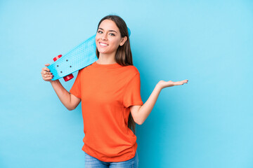 Young caucasian skater woman isolated showing a copy space on a palm and holding another hand on waist.