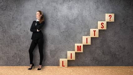businesswoman standing beside wooden cubes formed as a stair with the word LIMITS? on concrete background