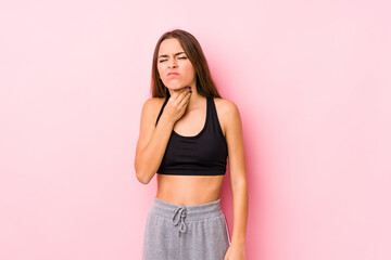 Young caucasian fitness woman posing in a pink background suffers pain in throat due a virus or infection.