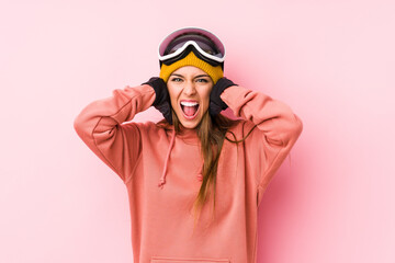 Young caucasian woman wearing a ski clothes isolated covering ears with hands trying not to hear too loud sound.