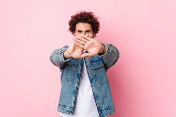 Curly mature man wearing a denim jacket against pink background doing a denial gesture