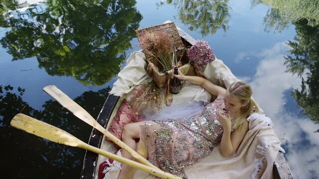 Luxury woman laying in rowboat smiling cheeky at camera and drinking champagne