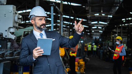 industrial manager in suit and wearing white protect helmet, check and control worker with tablet...