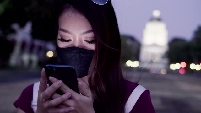 Woman with facemask uses phone in front of capitol building at night time