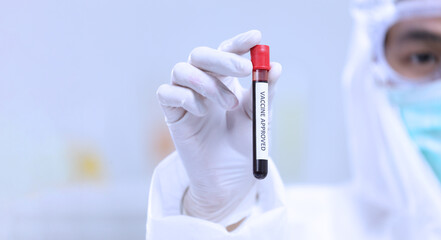 Science researcher in full protection equipment is holding a flask of approved vaccine with copy space