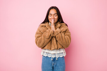 Young mixed race indian woman wearing a short sheepskin coatholding hands in pray near mouth, feels confident.