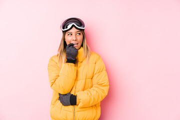 Young caucasian woman wearing a ski clothes in a pink background relaxed thinking about something looking at a copy space.