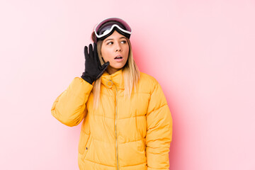 Young caucasian woman wearing a ski clothes in a pink background trying to listening a gossip.